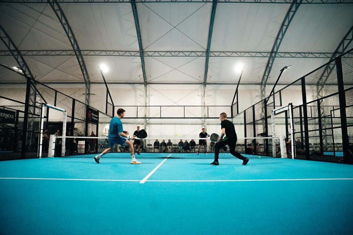 Doubles match in a large indoor hall, players at the net