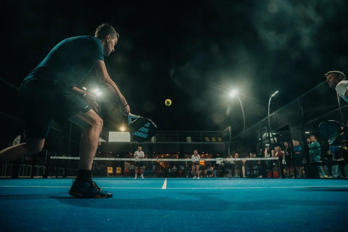 Player bending low for a return on a floodlit outdoor court at night